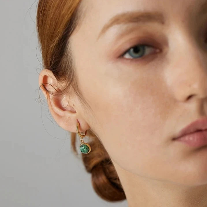 The Green Stone Charm Hoop Earrings exude majesty and elegance, reminiscent of the legendary stone of the African queen. Each green stone is delicately cut to enhance its natural beauty and vibrant hue, adding a touch of exoticism and sophistication to your look.