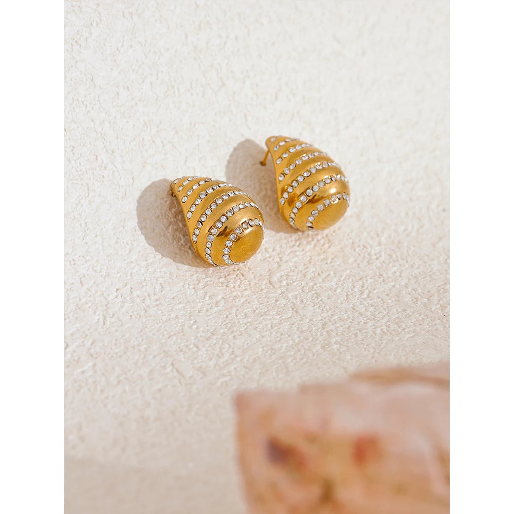 The "Row of Zirconia Drop Shape" earrings feature a classic drop design adorned with a row of meticulously secured zirconias, each set to sparkle beautifully. Crafted from hypoallergenic, eco-friendly stainless steel with a durable 18k gold plating, they offer both elegance and sustainability for the environmentally conscious wearer.