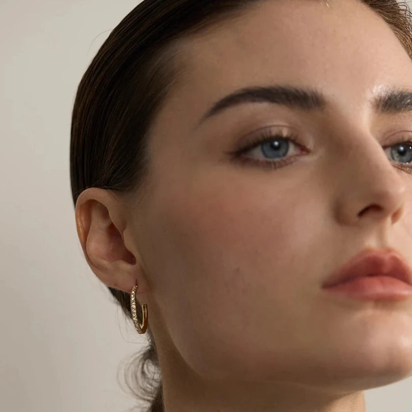 Stylish model wearing Shiny Zirconia Earrings with C-shaped Hoops, highlighting their versatile design and contemporary elegance, made from sustainable stainless steel with 18k gold plating.